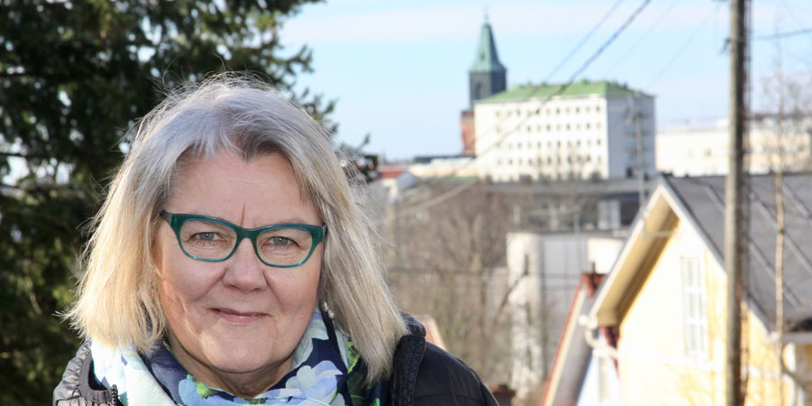 Helena Leino-Kilpi ulkona Tyksin mäellä, taustalla näkyy mm. tuomiokirkon torni