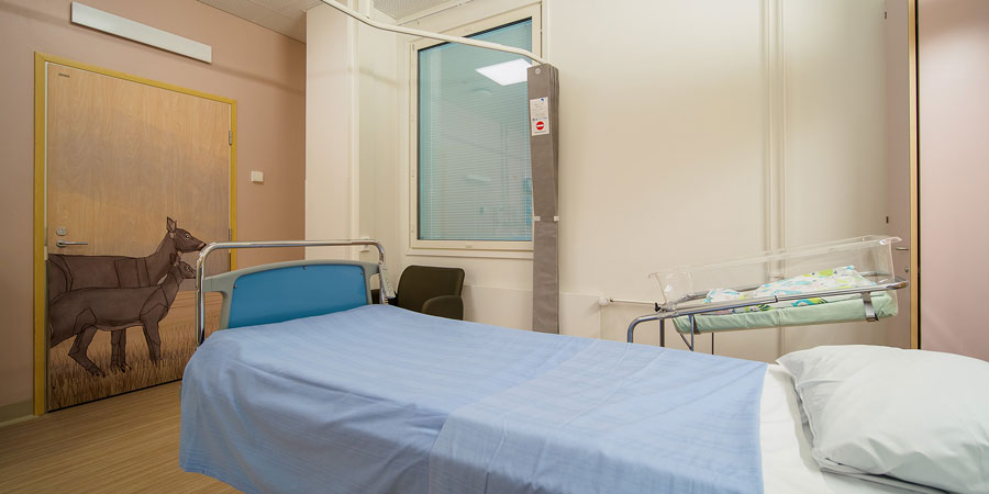 Rum med en patient säng och en baby säng, på dörren en bild av två rådjur.