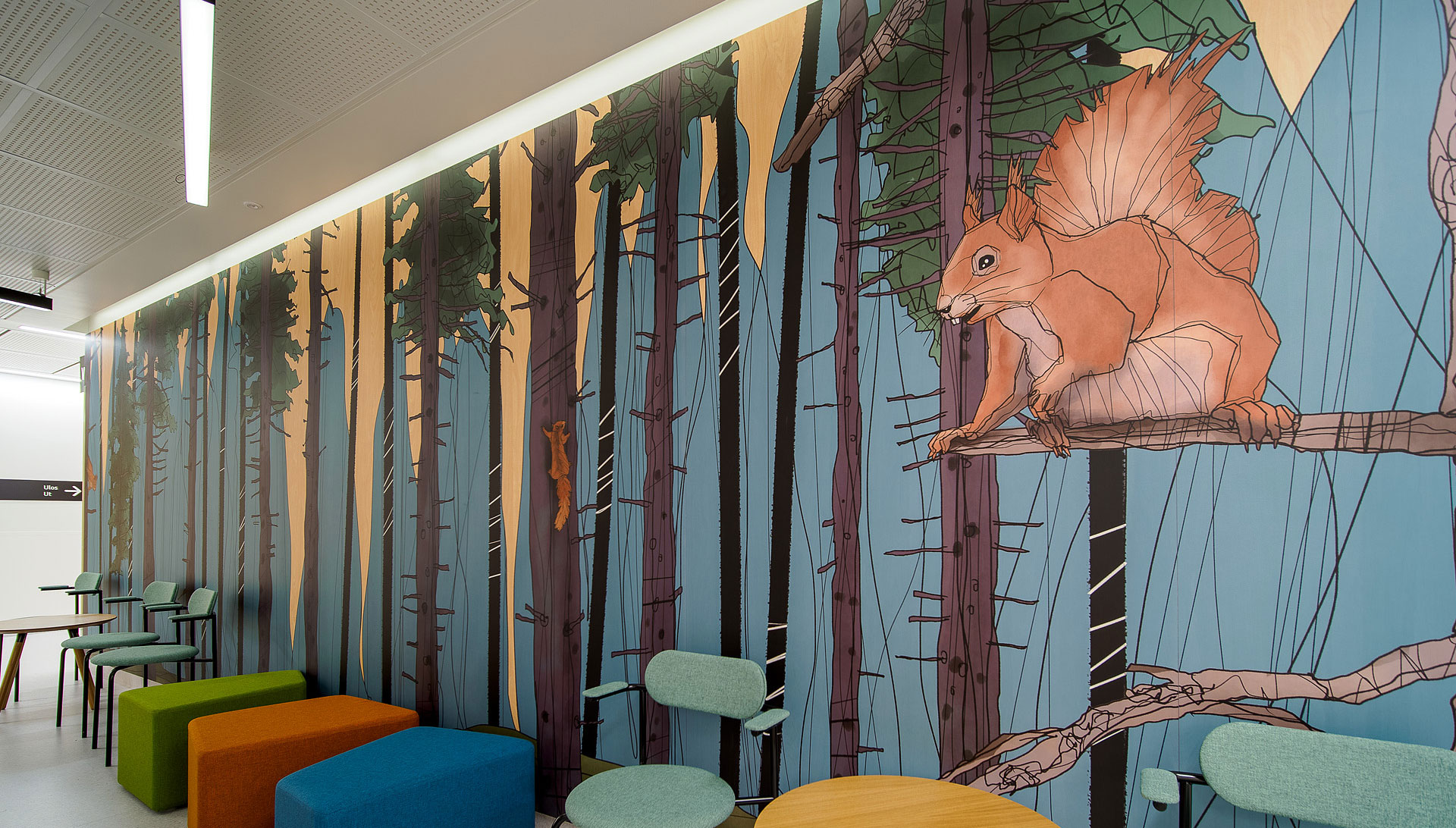 Osa huonetta, jonka seinään maalattu metsää ja oravia. Seinän edessä värikkäitä istuimia.