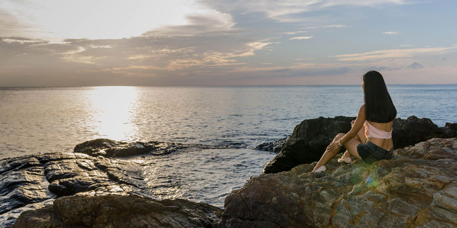 Nainen istuu kalliolla meren rannalla.
