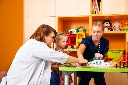 Lääkäri ja hoitaja leikkivät lapsen kanssa.