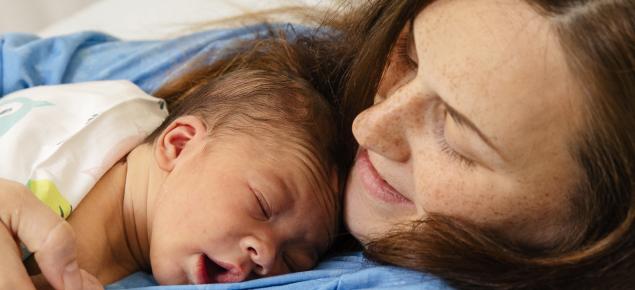 En mamma håller ett nyfött barn i sina armar.