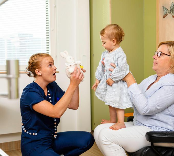 A child is on her mother's lap. Nurse gives the child a bunny toy.