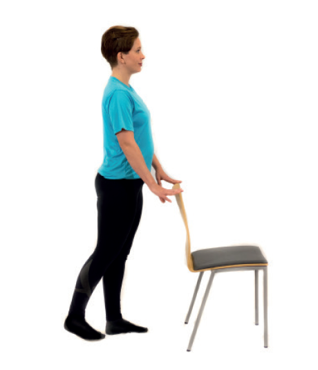 nainen seisoo pitäen tuolin selkänojasta kiinni.