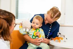 Ett litet barn sitter i sjukskötares famnen. Läkare tittar på barnet.